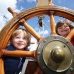 kids playing with the steering wheel on a boat